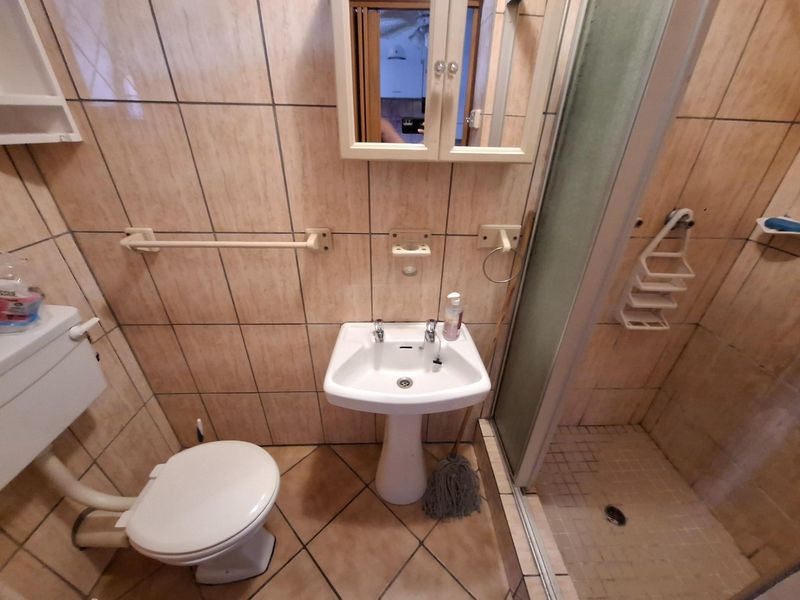 A compact bathroom featuring a pedestal sink, a toilet, and a glass-enclosed shower stall with neutral wall and floor tiling.