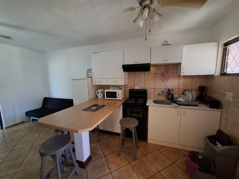 Compact open-plan kitchen featuring white cabinetry, a built-in breakfast bar, tiled backsplash, and a freestanding stove, integrated with a small living area.