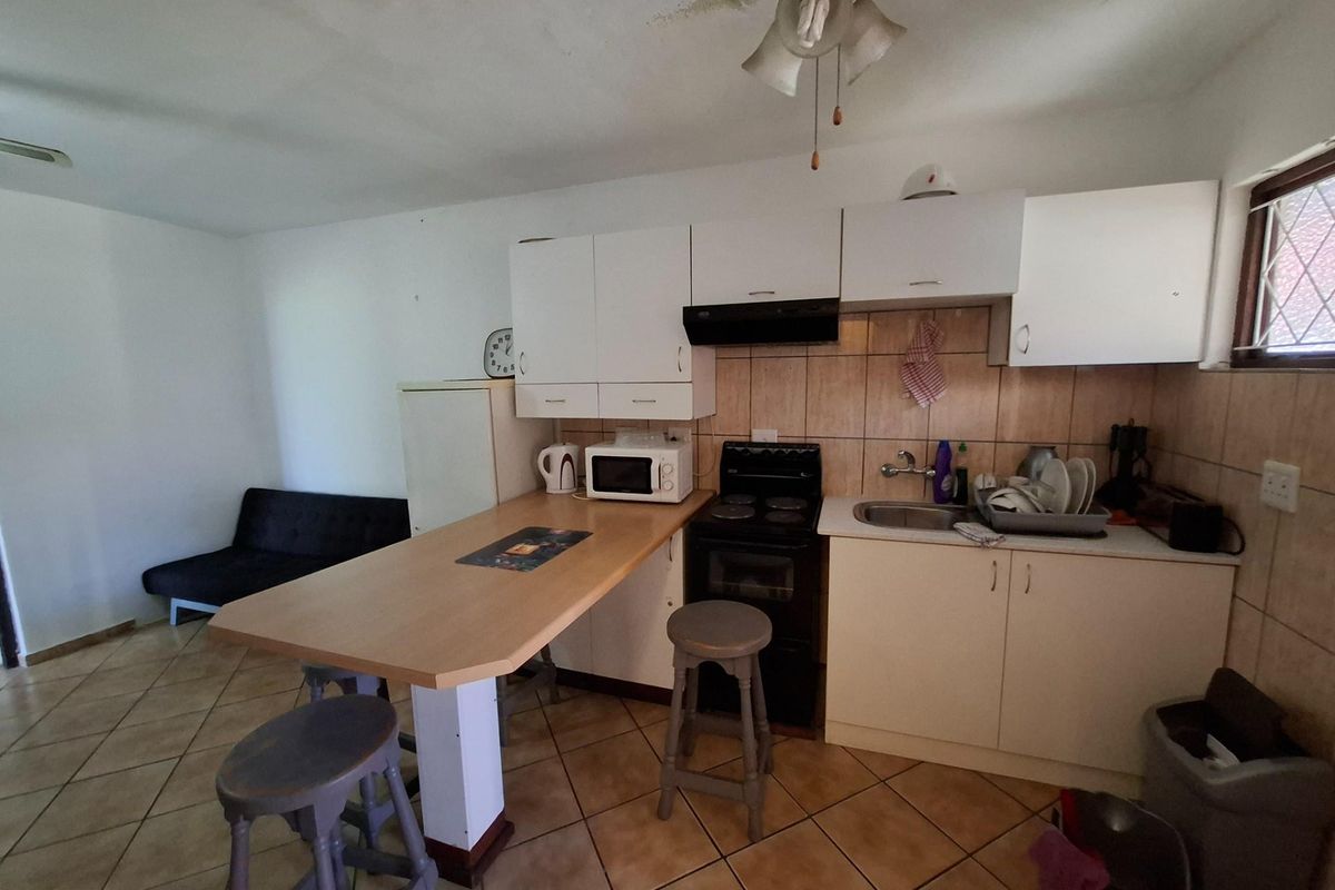 Compact open-plan kitchen featuring white cabinetry, a built-in breakfast bar, tiled backsplash, and a freestanding stove, integrated with a small living area.