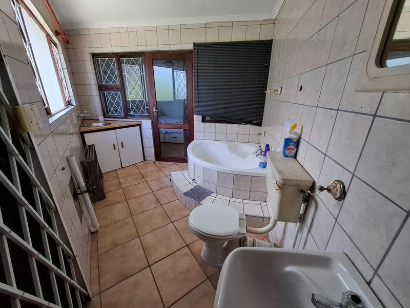 A dated bathroom featuring a corner bathtub, pedestal basin, and toilet, with tiled walls and flooring, requiring modernization and cosmetic updates.