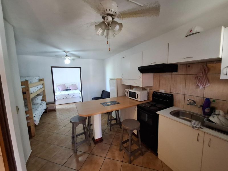 Open-plan kitchen and living area featuring tiled flooring, built-in cabinetry, and a breakfast counter, with an adjacent bedroom visible.