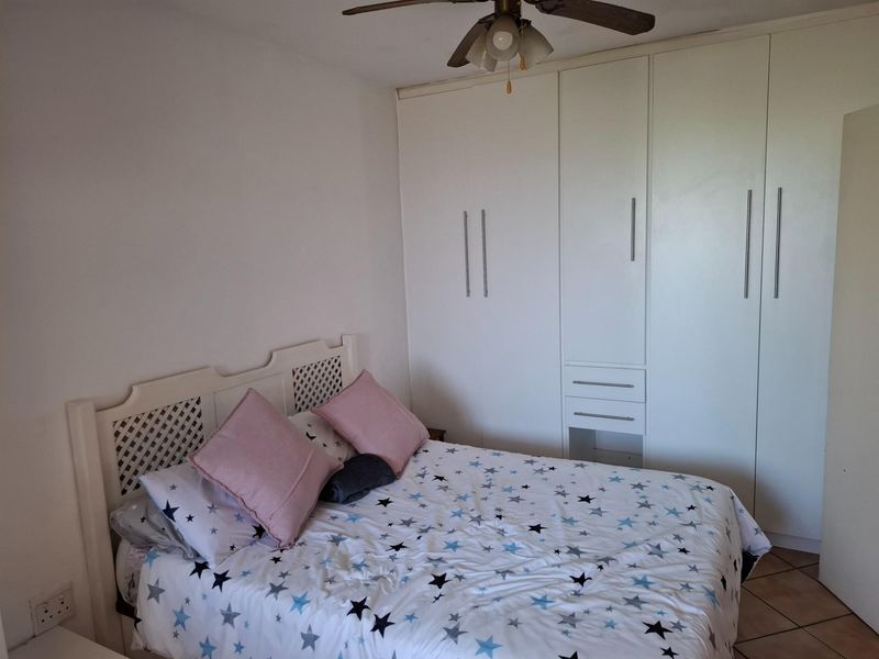 A bedroom featuring built-in white cabinetry with integrated drawers and a ceiling fan.