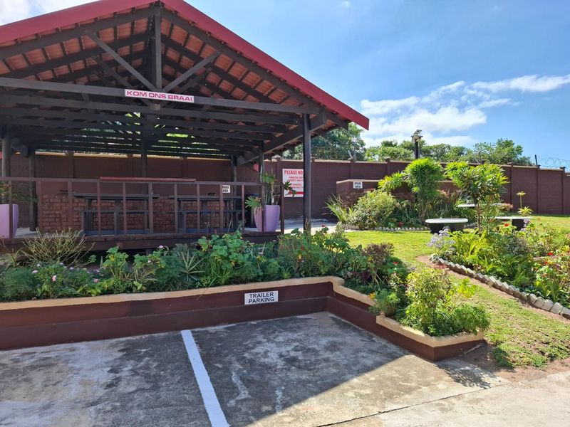 Outdoor communal braai area featuring a covered timber gazebo, landscaped garden beds, and designated trailer parking space within a secure complex.