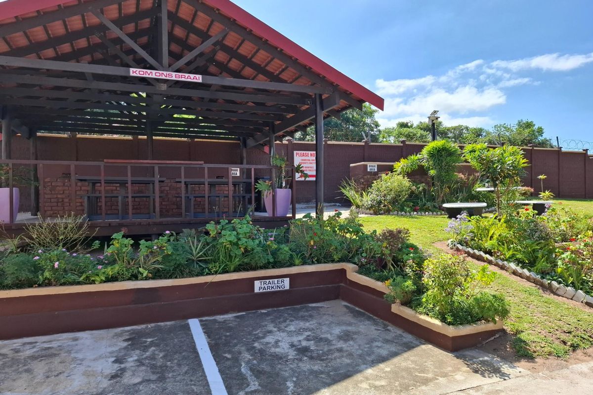 Outdoor communal braai area featuring a covered timber gazebo, landscaped garden beds, and designated trailer parking space within a secure complex.