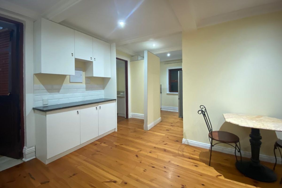 A functional kitchen area featuring white cabinetry, dark countertops, and warm timber flooring, leading into an adjacent room.