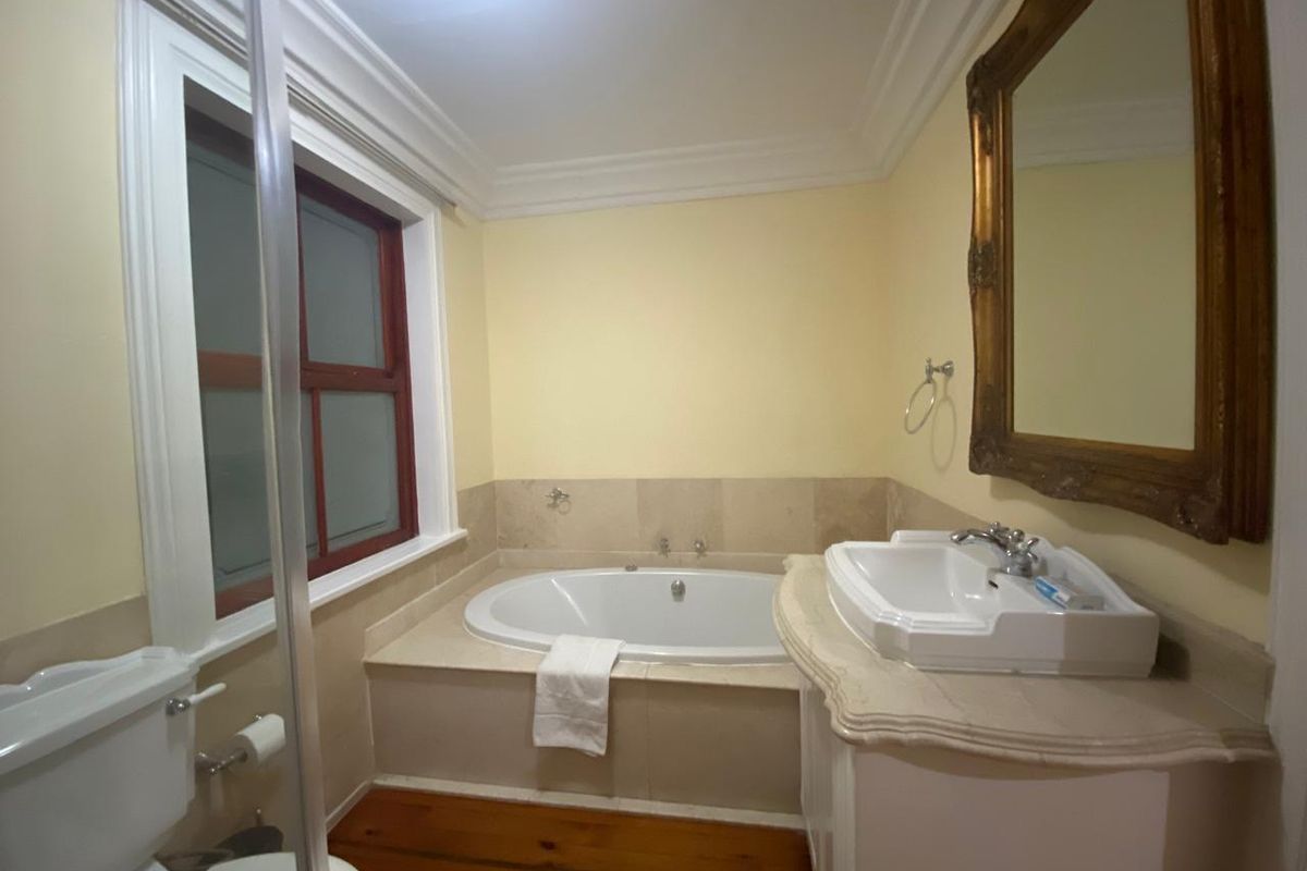 A bathroom featuring a built-in bathtub, a vanity with a basin, and a toilet, finished with wooden flooring and neutral wall tones.