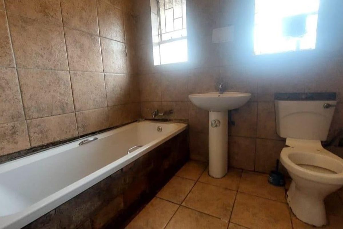 A functional bathroom featuring a built-in bathtub, pedestal basin, and toilet, finished with full-height wall tiling and floor tiles.