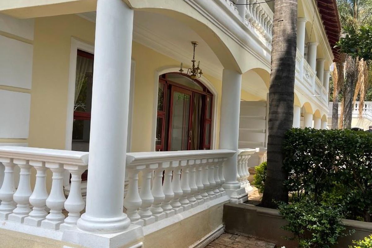 A classic exterior view of the apartment building featuring a covered patio with decorative balustrades, arched architectural details, and a paved garden walkway.