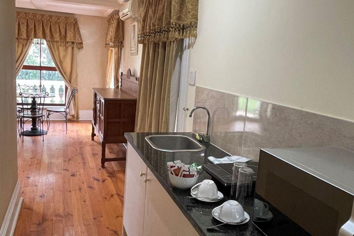 A compact kitchenette area featuring granite countertops, a stainless steel sink, and built-in cabinetry, flowing into an adjacent living space with timber flooring.