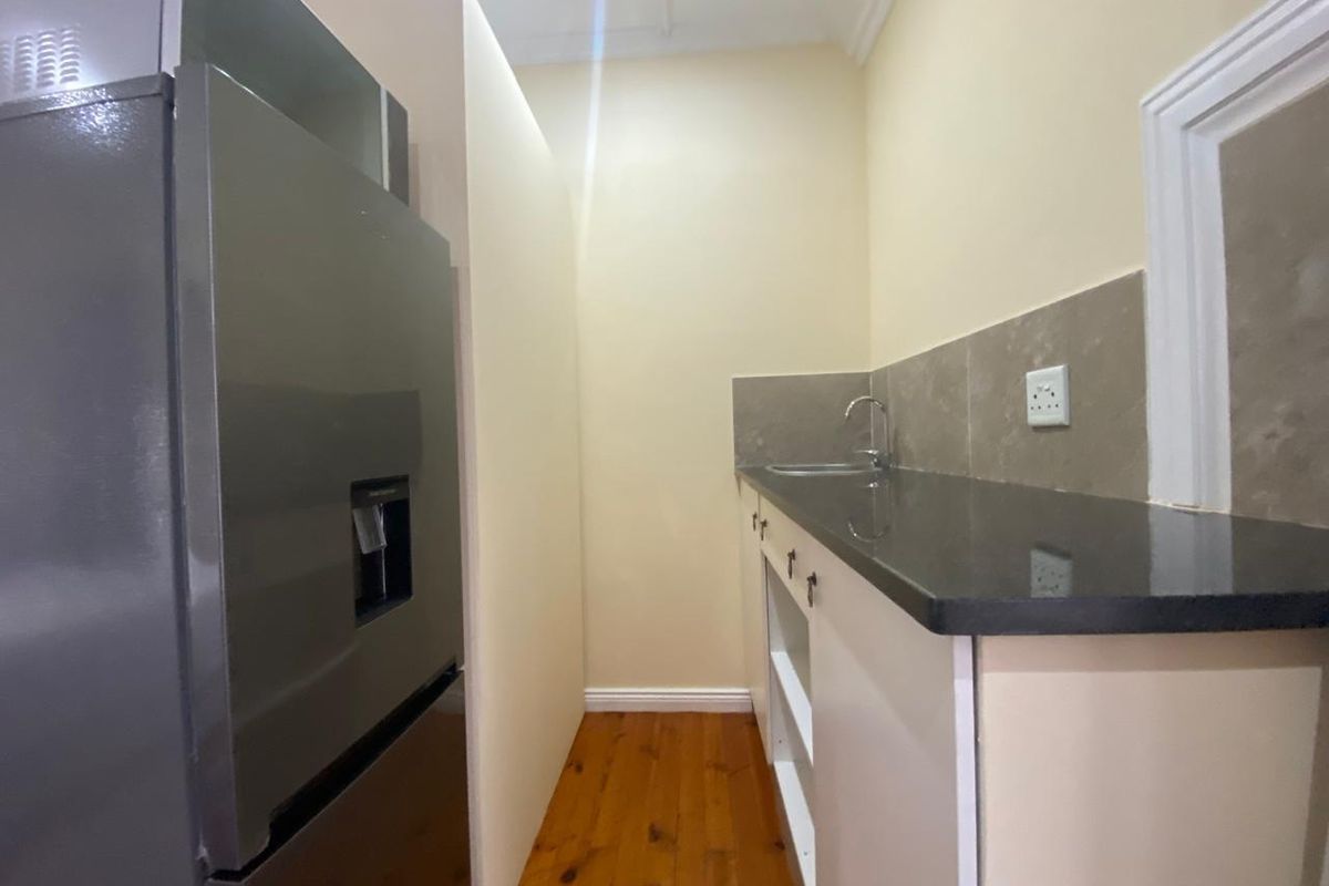 A compact kitchen area featuring dark stone countertops, a stainless steel sink, tiled backsplash, and wooden flooring.