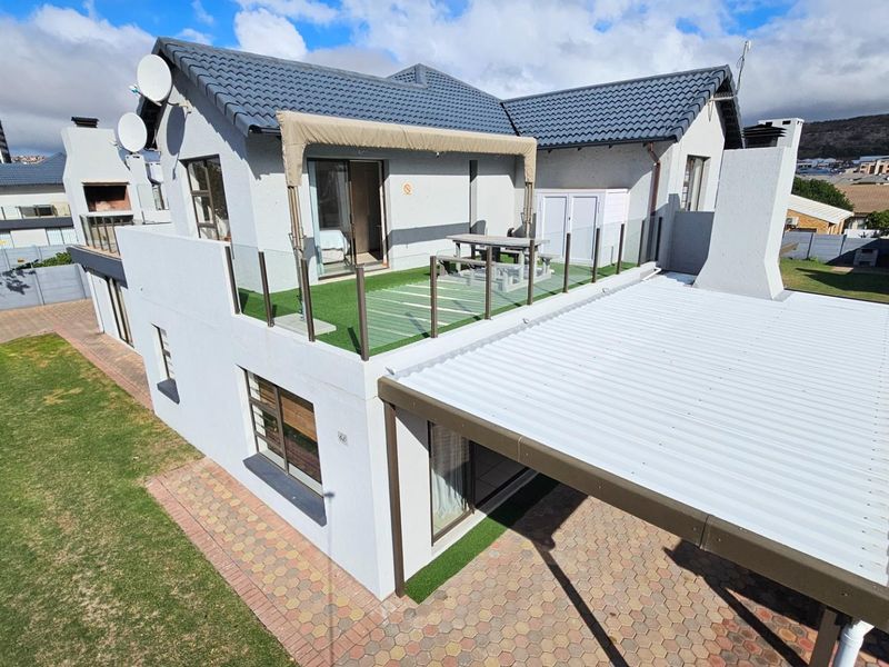 An elevated view of the rear exterior featuring a tiled roof, a spacious balcony with glass balustrades, and a paved patio area with a covered roof.