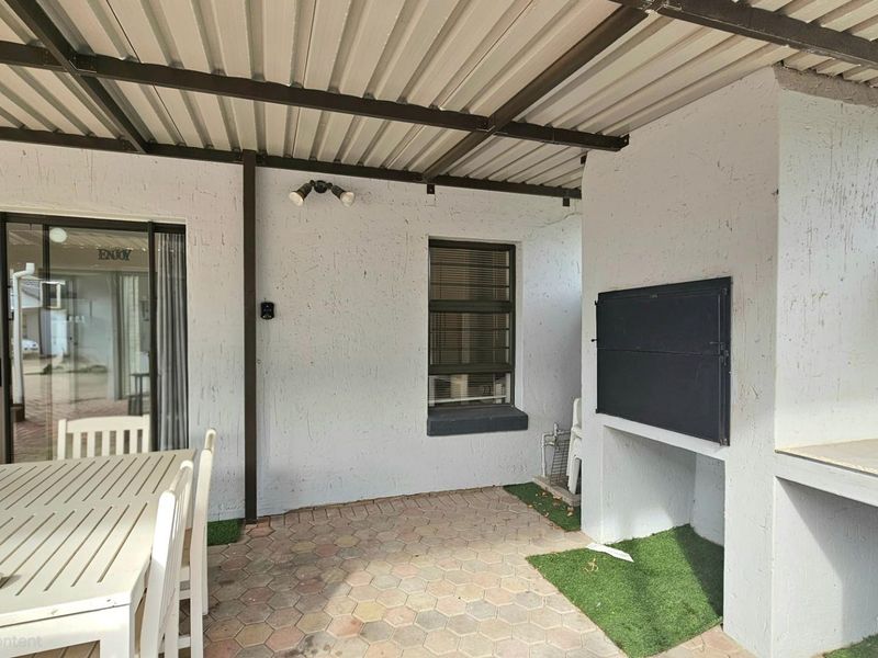 Covered patio area featuring a built-in braai, paved flooring, and direct access to the interior living space through sliding glass doors.