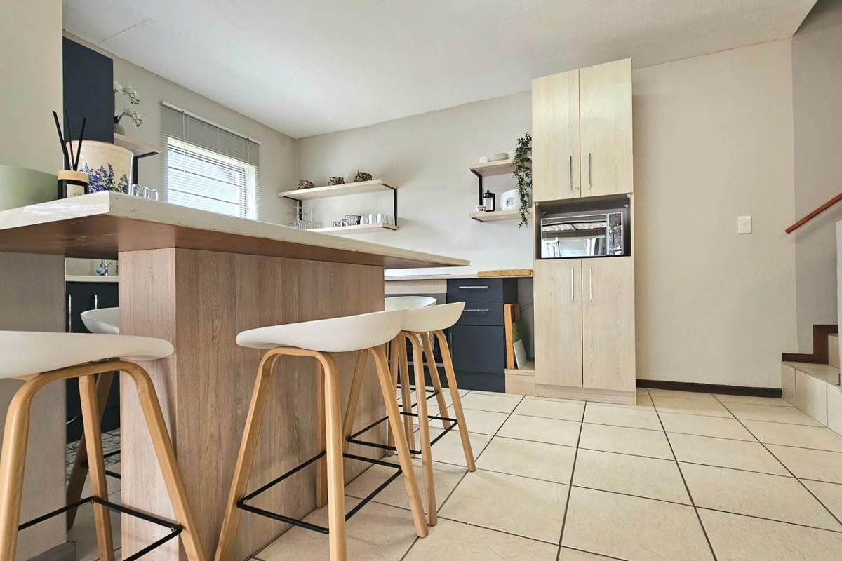 Modern kitchen featuring a breakfast bar, light wood-tone cabinetry, built-in microwave, and tiled flooring, offering a functional and contemporary cooking space.