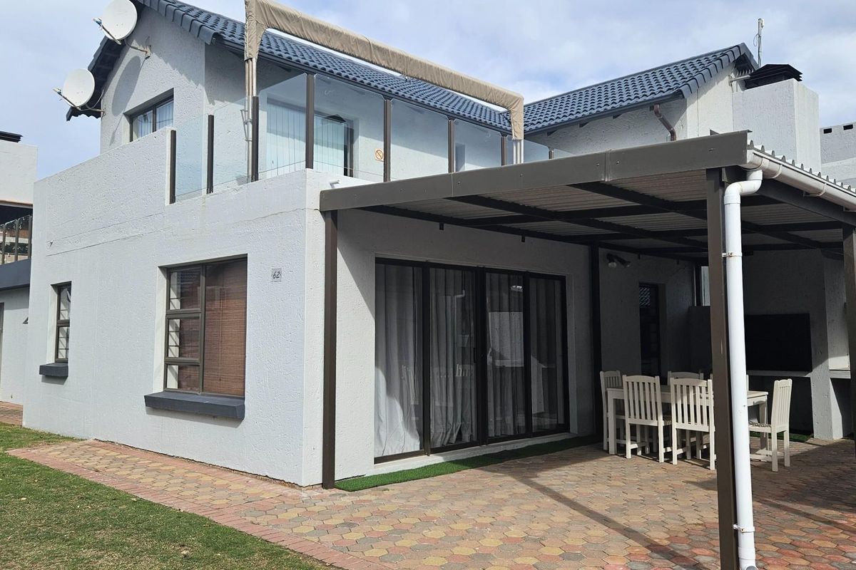 Rear view of the property featuring a paved patio area with a covered pergola, glass balcony railing, and exterior access doors.