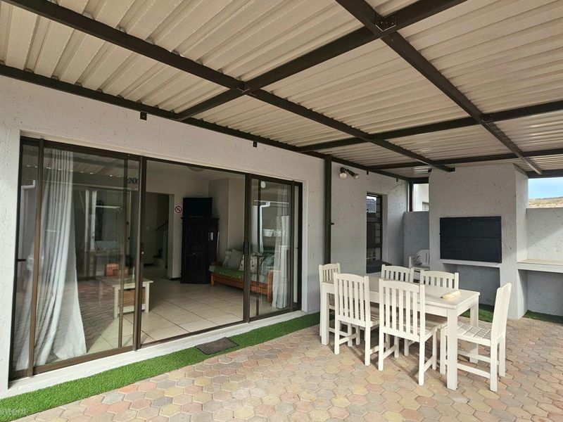 Covered patio area featuring a built-in braai, paved flooring, and sliding door access to the interior living space.