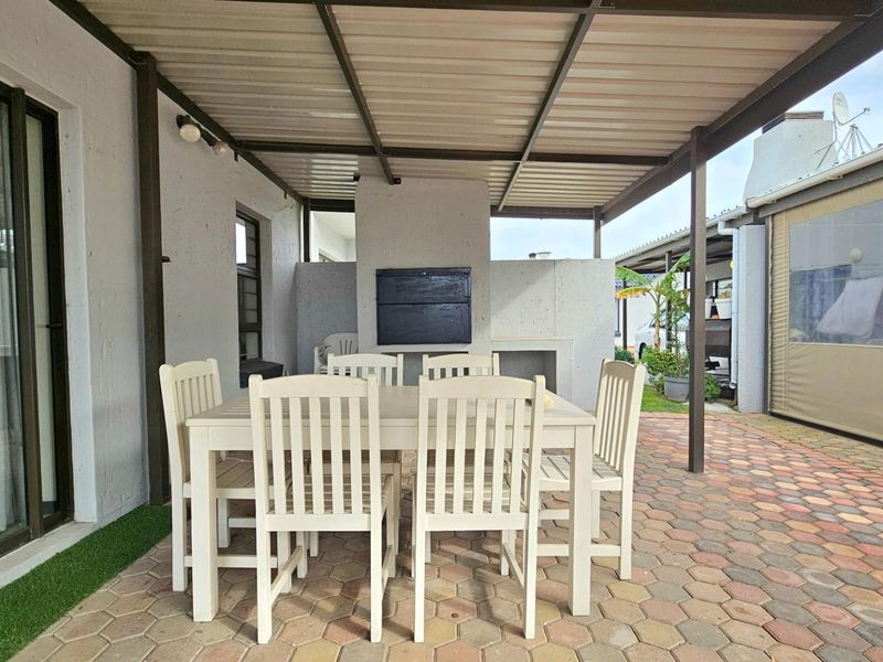 Covered patio area featuring a built-in braai, paved flooring, and direct access to the interior living space through sliding glass doors.