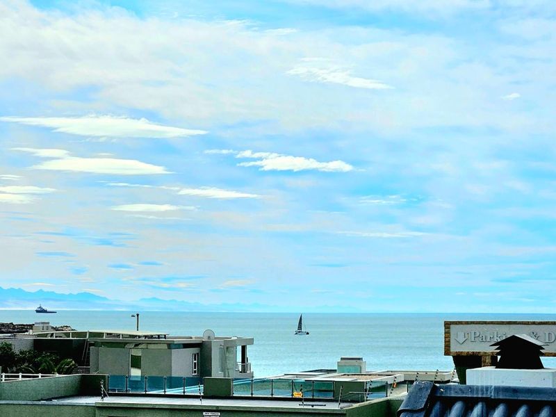 Elevated view overlooking the ocean and surrounding coastal neighborhood, capturing a scenic horizon and distant mountain range.