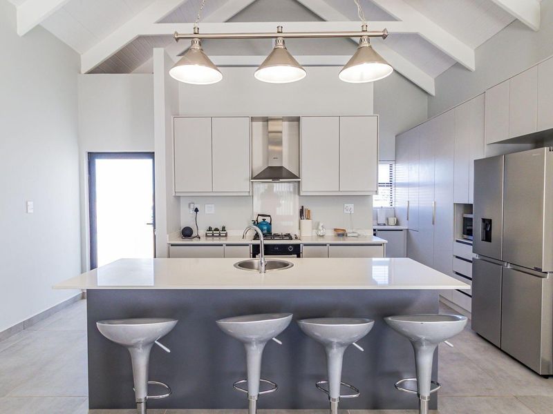 Modern kitchen featuring a central island with sink, sleek cabinetry, vaulted ceilings, and contemporary pendant lighting in a bright, open-plan layout.