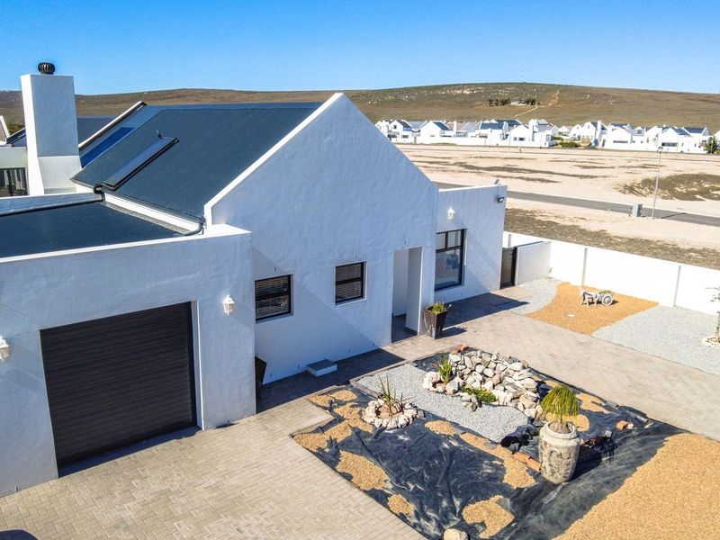 Aerial view of a modern white house featuring a metal roof, solar water heater, attached garage, and an ongoing landscaping project in the front yard.