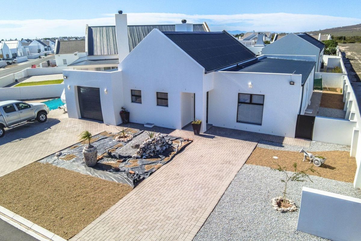 Aerial view of a modern white house with a metal roof, paved driveway, and enclosed garden area in a residential estate.