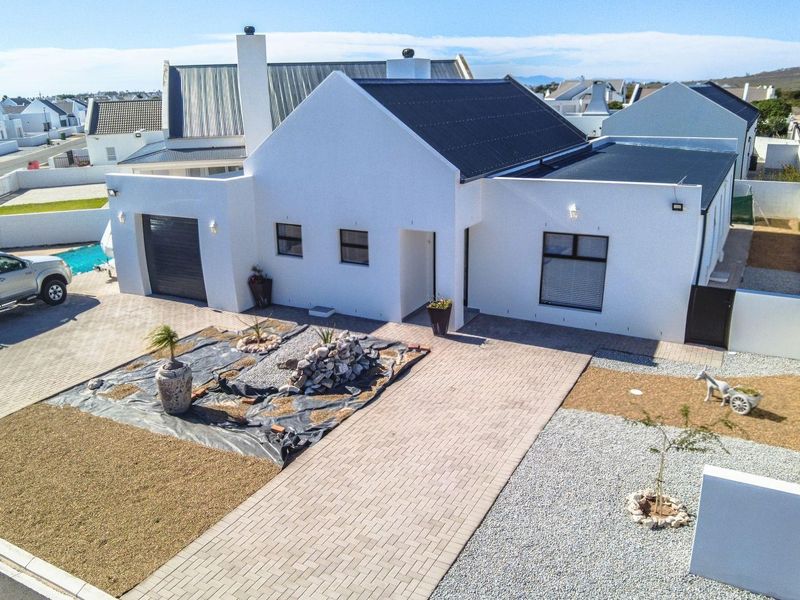Aerial view of a modern white house with a metal roof, paved driveway, and enclosed garden area in a residential estate.