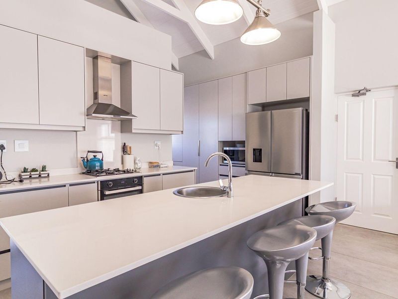 Modern kitchen featuring a central island with sink, sleek cabinetry, gas hob, extractor fan, and vaulted ceilings for an airy, contemporary feel.