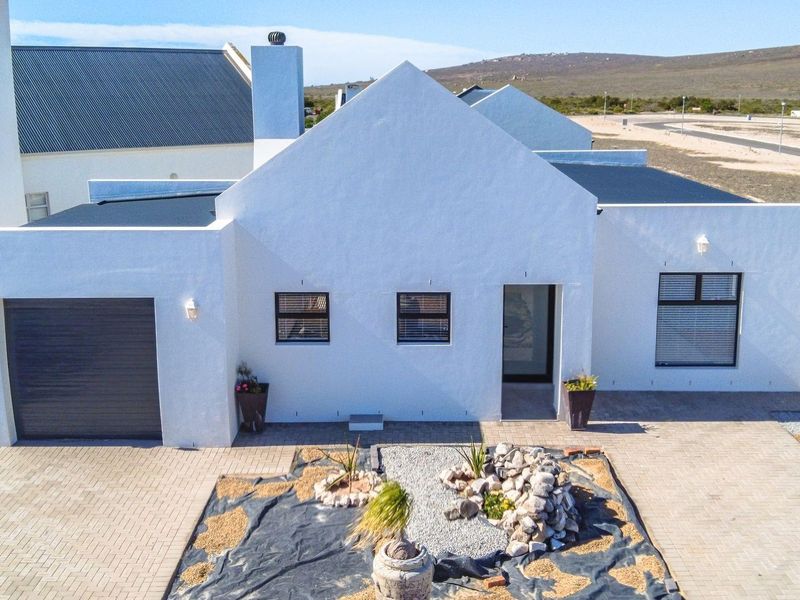 Aerial view of the front facade featuring a white rendered finish, integrated garage, and a landscaped rock garden area.