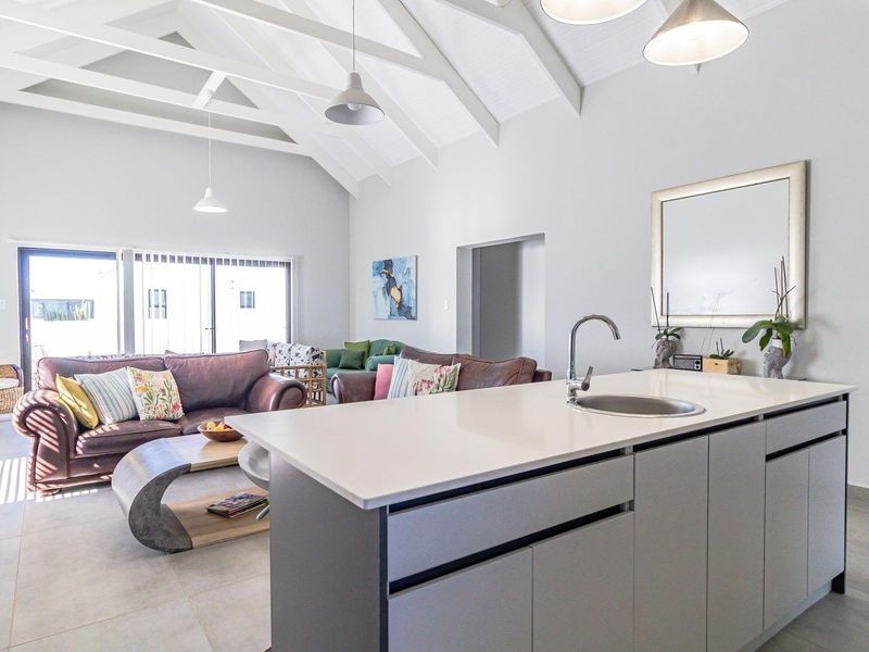 Spacious open-plan living area featuring a modern kitchen island with sink, vaulted ceilings with exposed rafters, and large sliding doors leading outdoors.