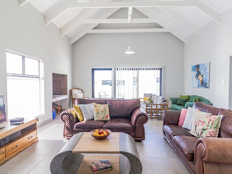 Spacious living room featuring a high vaulted ceiling with exposed trusses, tiled flooring, and a built-in fireplace, opening to an outdoor area.