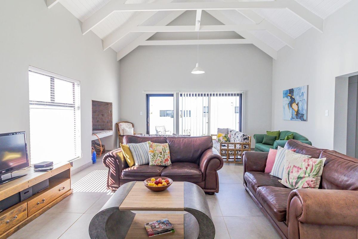 Spacious living room featuring a high vaulted ceiling with exposed trusses, tiled flooring, and a built-in fireplace, opening to an outdoor area.