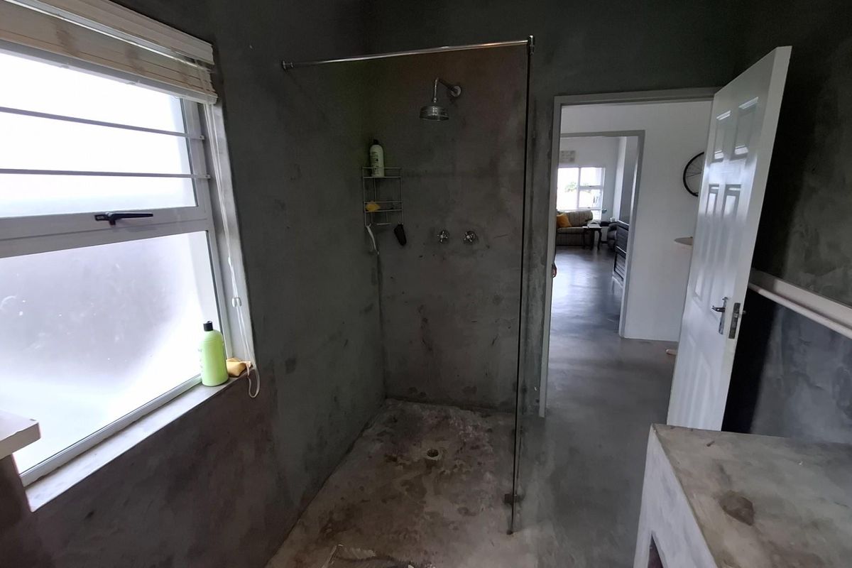 A bathroom featuring an open-concept walk-in shower with a glass screen and raw concrete wall finishes, currently in need of cosmetic completion.