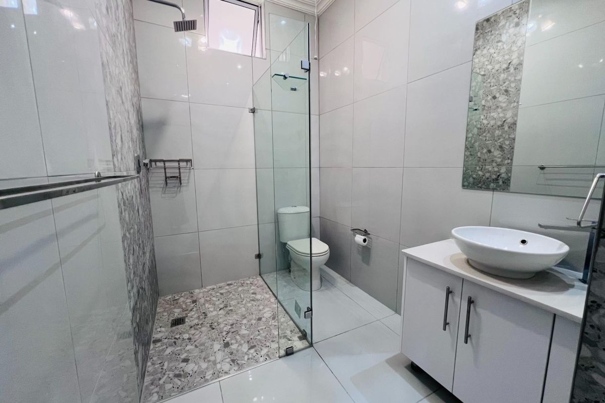 Modern bathroom featuring a walk-in shower with glass screen, rain shower head, vessel sink vanity, and contemporary tiled finishes.