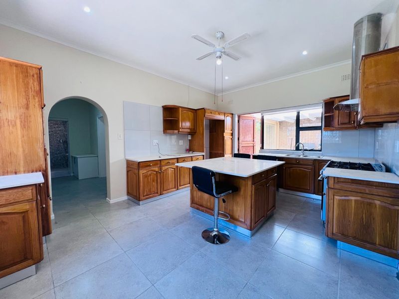 Spacious kitchen featuring wooden cabinetry, stone countertops, a central island, and a gas hob, with tiled flooring and an arched entryway.