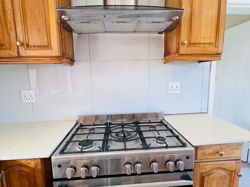 A kitchen area featuring wooden cabinetry, a stainless steel gas stove with an extractor fan, and a tiled backsplash.