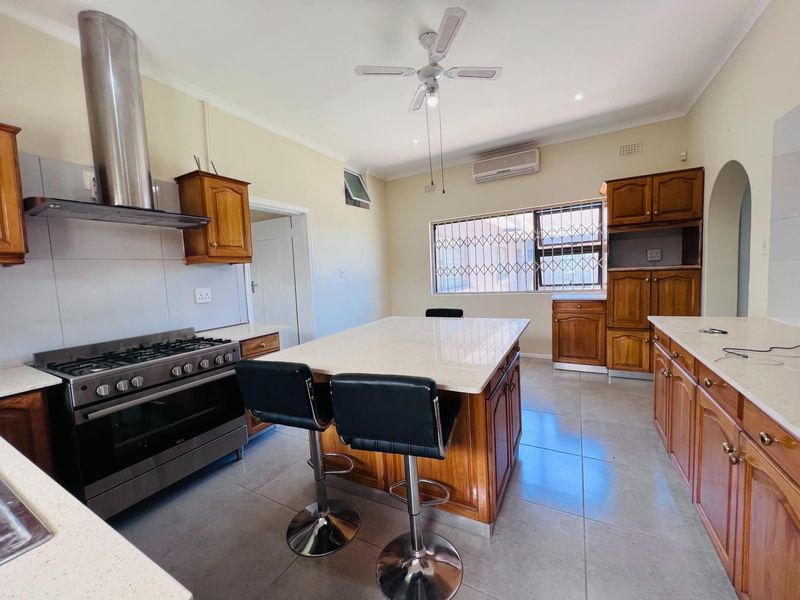 Spacious kitchen featuring wooden cabinetry, stone countertops, a central island, and a stainless steel gas stove with an extractor fan.