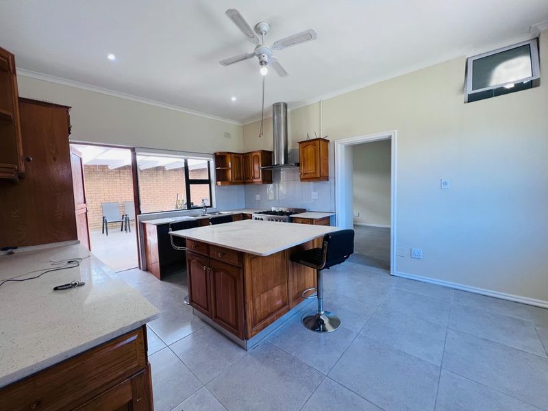 A functional kitchen featuring wooden cabinetry, a central island with stone countertop, gas hob, extractor fan, and direct access to an outdoor patio area.