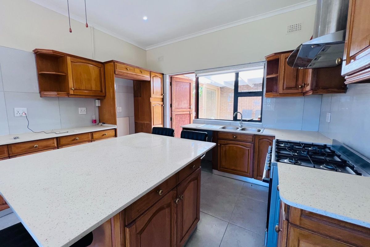 A spacious kitchen featuring traditional wooden cabinetry, stone countertops, a central island, and a gas hob with an extractor fan.