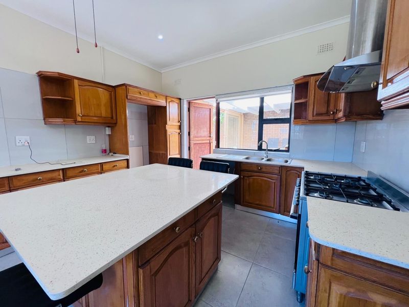 A spacious kitchen featuring traditional wooden cabinetry, stone countertops, a central island, and a gas hob with an extractor fan.