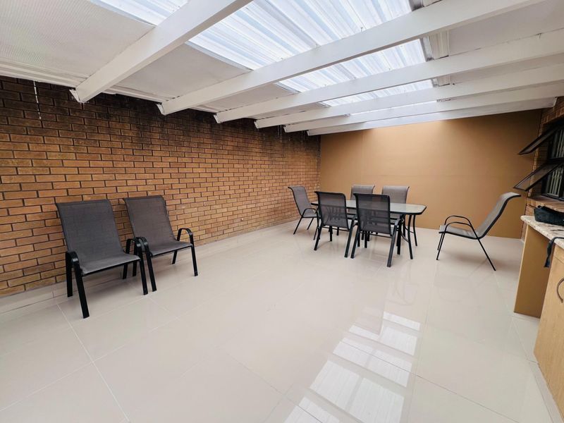 Covered outdoor patio featuring tiled flooring, an exposed brick wall, and a built-in counter area, providing a functional space for outdoor dining and relaxation.