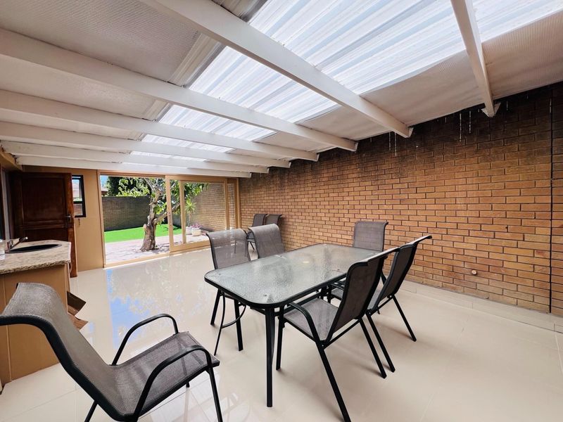 Covered patio area featuring a translucent roof, exposed brick wall, and tiled flooring, providing a seamless transition to the outdoor garden space.