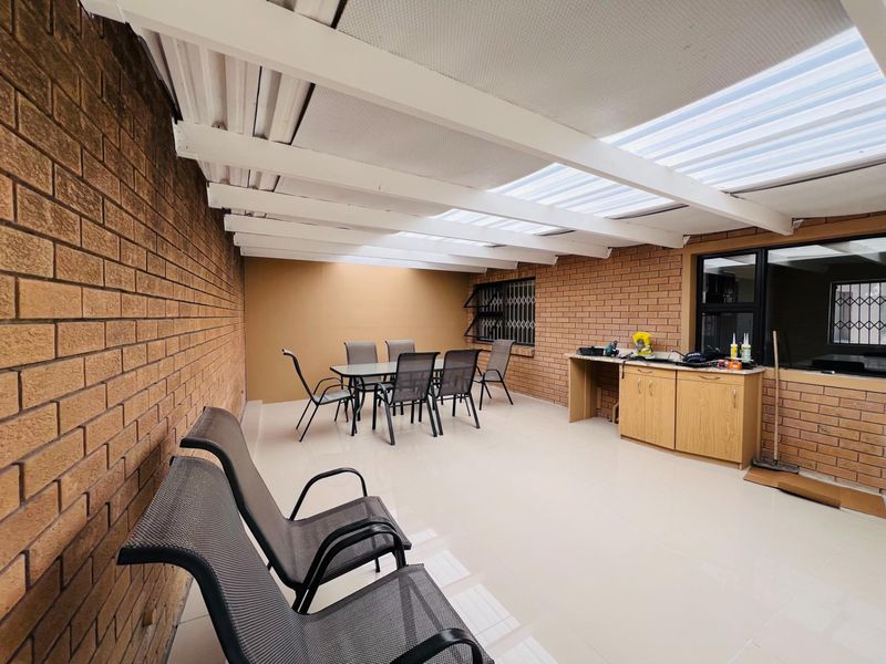 Covered outdoor patio featuring a translucent roof, tiled flooring, brick walls, and built-in cabinetry, ideal for alfresco dining and entertaining.