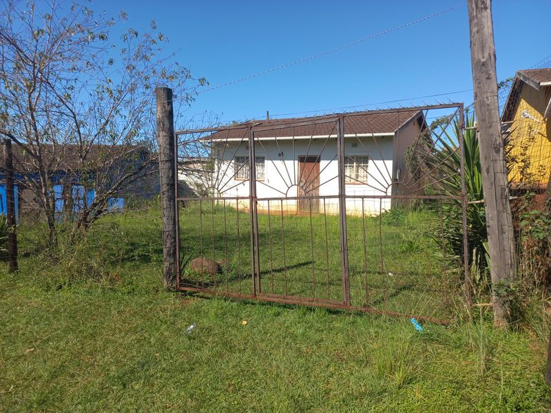Front view of a modest residential house featuring a metal security gate, tiled roof, and security bars on the windows, set on a grassy plot.