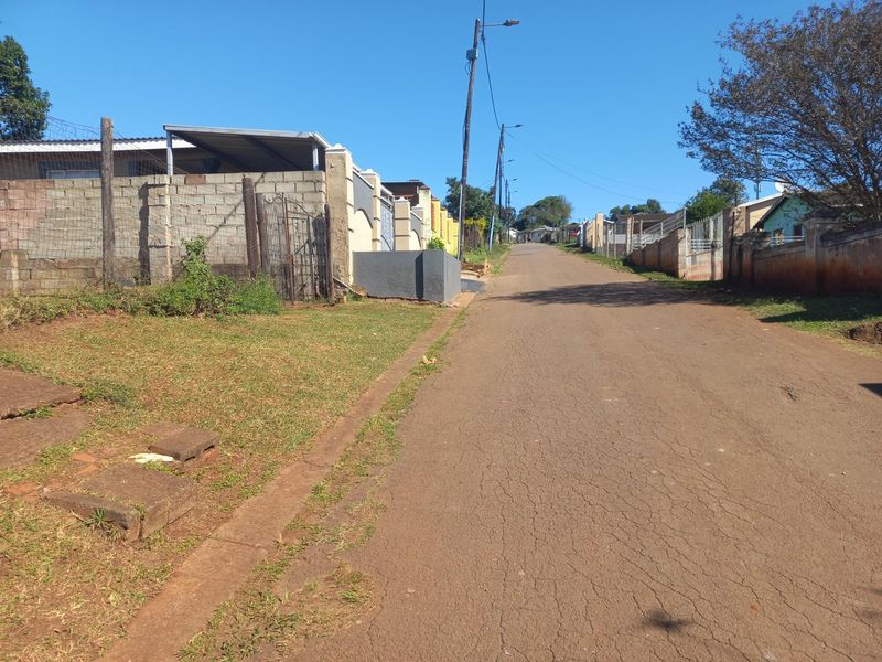 A street view showing the residential road approach with asphalt surfacing, concrete boundary walls, and overhead utility infrastructure.