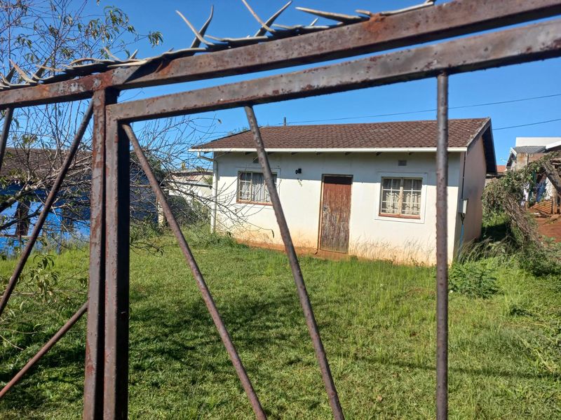 Front view of a single-story house featuring a tiled roof and security-fenced yard, showing signs of significant weathering and maintenance requirements.