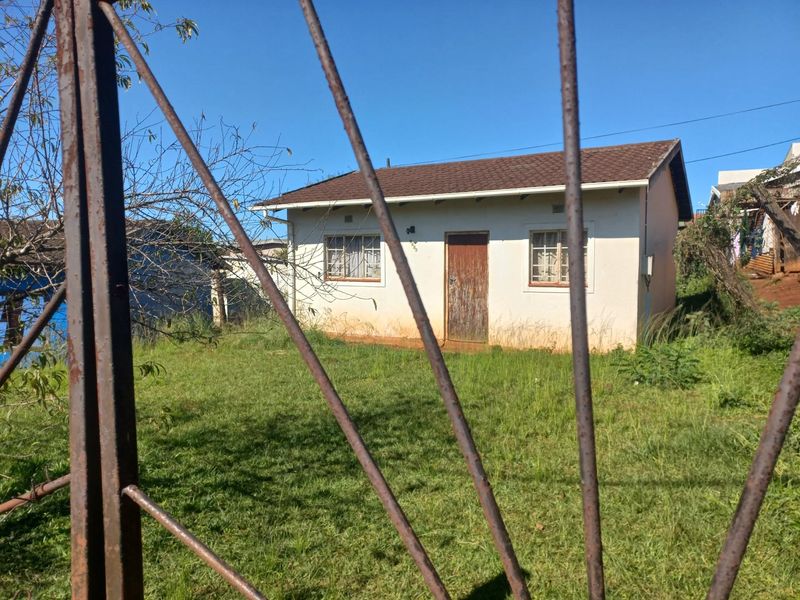 A detached single-story house viewed through a metal security gate, featuring a tiled roof and exterior walls in need of maintenance.
