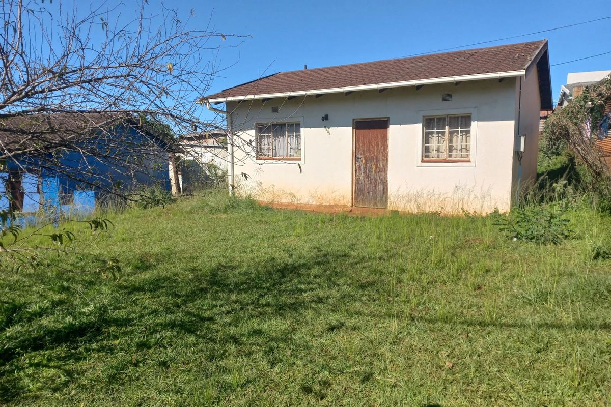 Rear view of a detached house featuring a tiled roof, plastered walls, and a large garden area requiring maintenance.