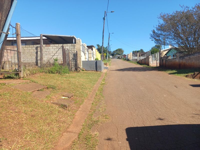 A street view showing the asphalt road, surrounding residential boundary walls, and utility infrastructure in a suburban neighborhood setting.