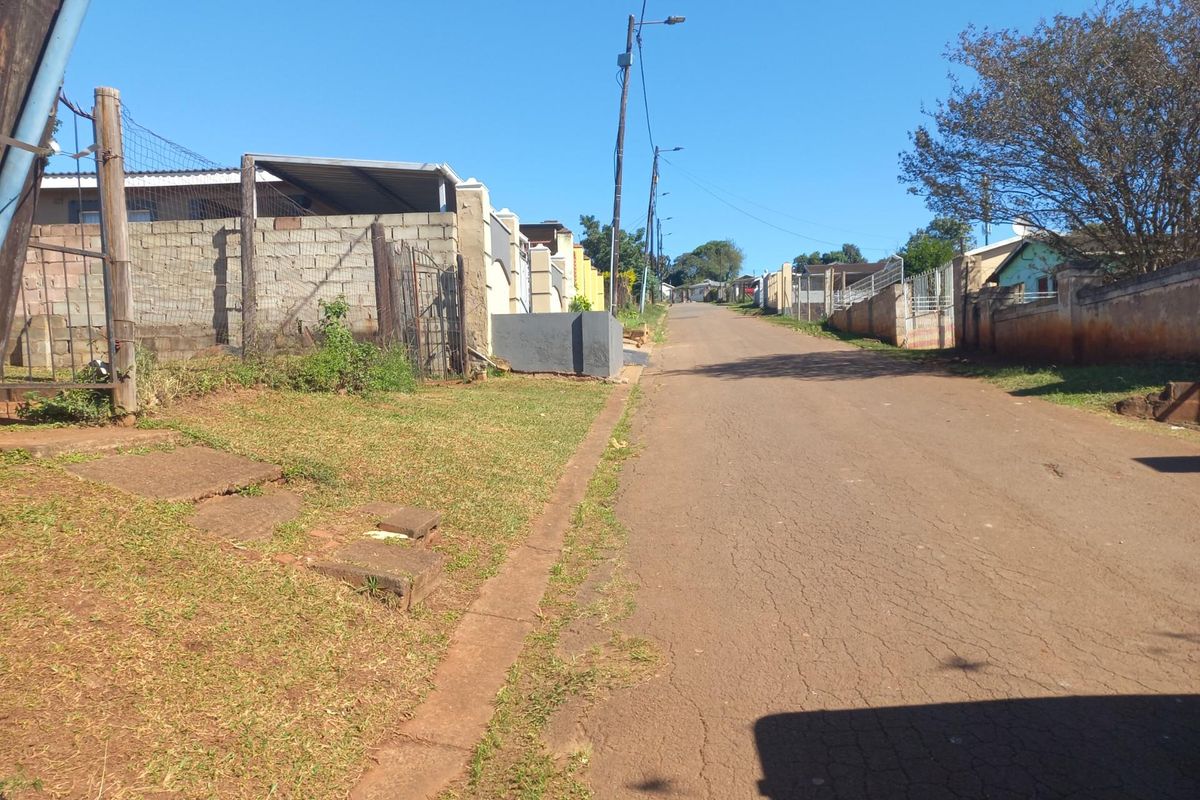 A street view showing the asphalt road, surrounding residential boundary walls, and utility infrastructure in a suburban neighborhood setting.