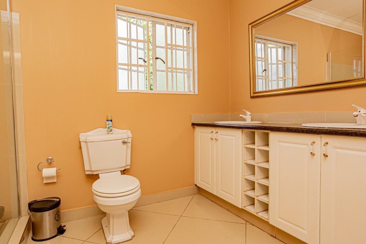 A functional bathroom featuring a double vanity with white cabinetry, a toilet, and a glass-enclosed shower with tiled flooring.