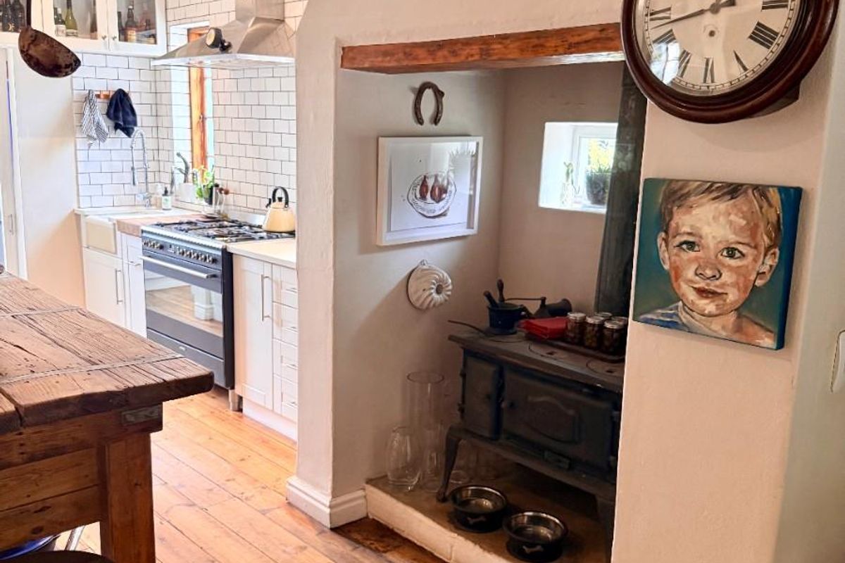 A charming kitchen featuring a built-in stove, subway tile backsplash, timber flooring, and a traditional fireplace hearth with a vintage-style wood-burning stove.